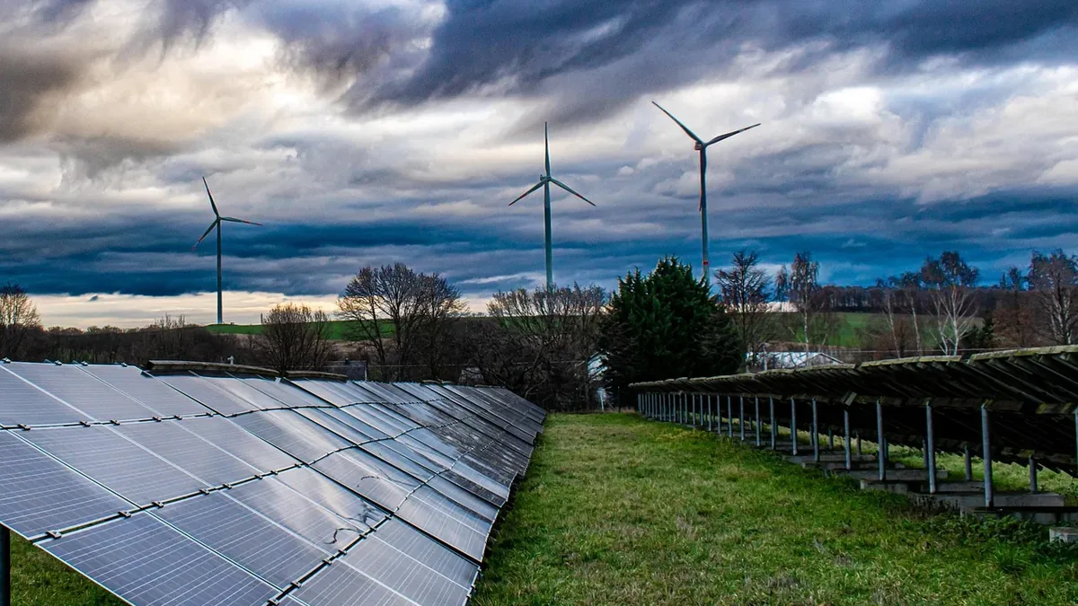 A solar panel array and wind turbines in a grassy field.