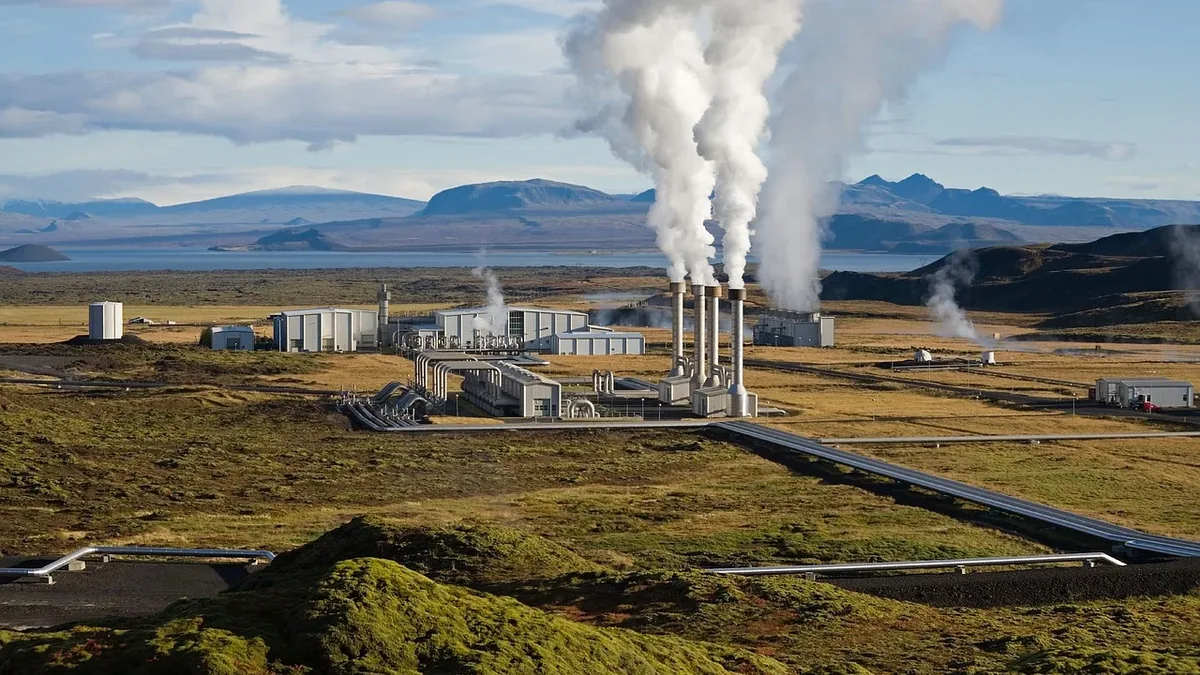 A geothermal power plant situated in a vast, open landscape with rolling hills and mountains in the background.