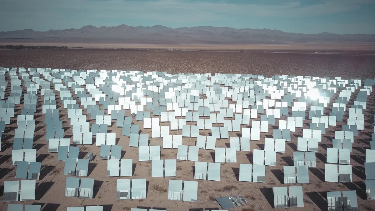 A large solar power plant with numerous rows of solar panels arranged in a grid pattern, situated in a desert landscape.