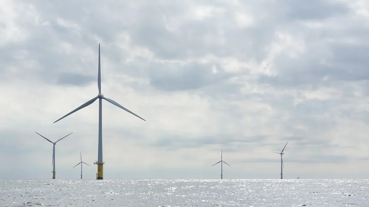 A group of wind turbines standing in the water, with one prominent turbine in the foreground and several others in the background.