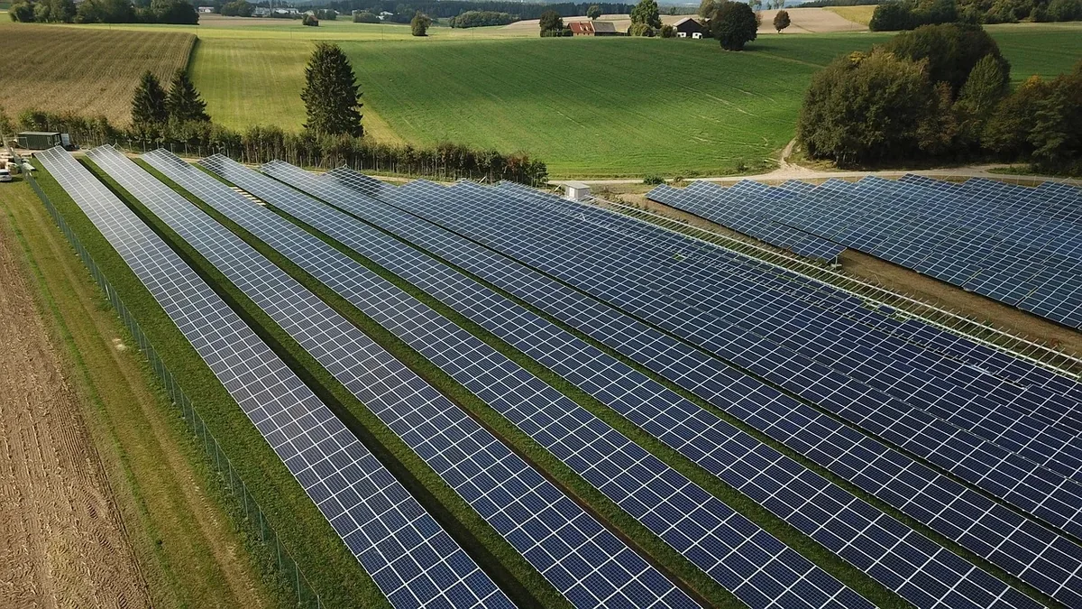 A large solar panel array situated in a rural area, comprising multiple rows of panels arranged in a grid pattern.
