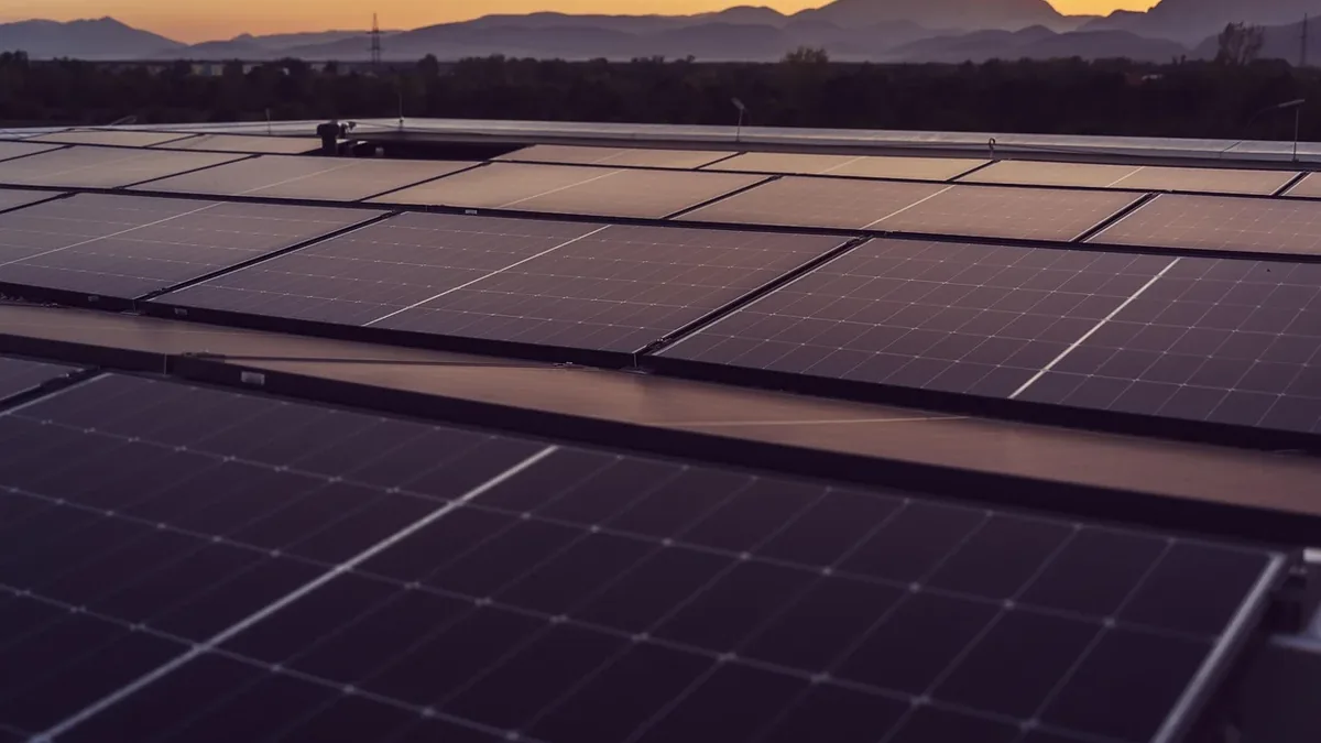 A rooftop covered with solar panels, set against a backdrop of mountains and trees.