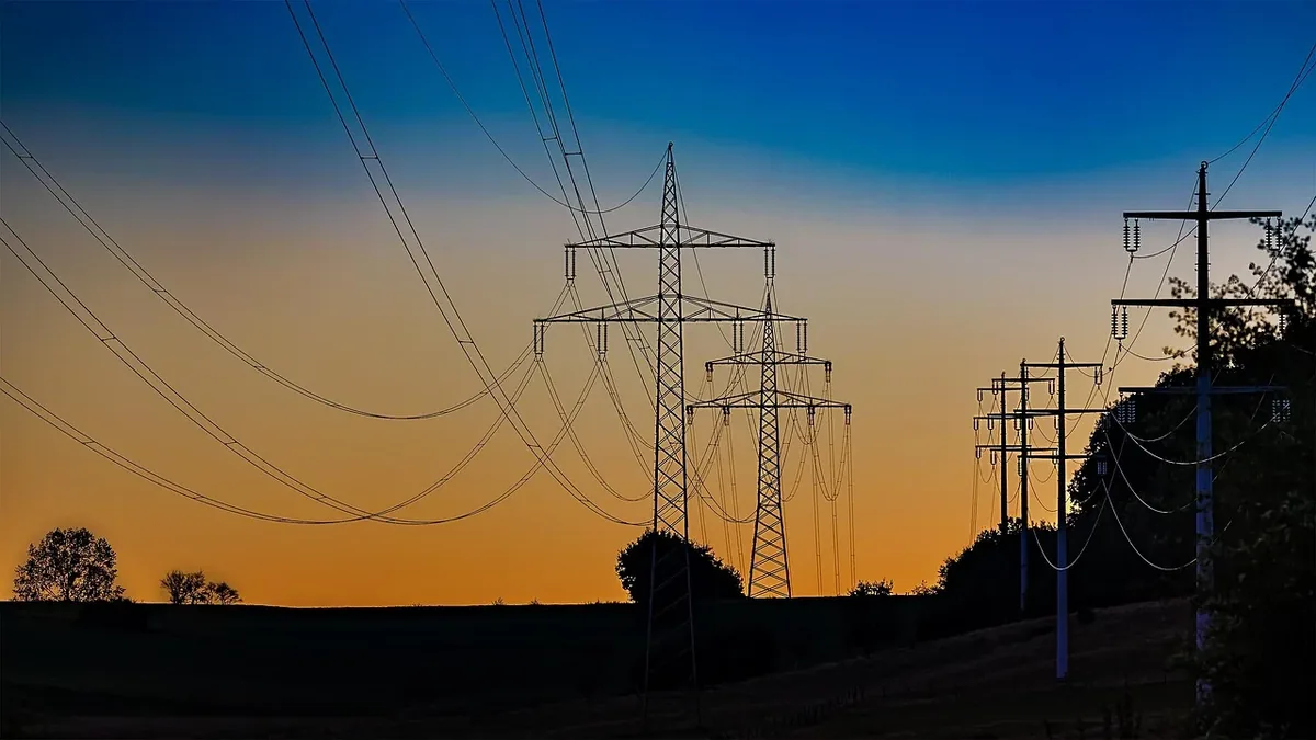 A row of power lines and transmission towers in a rural area at sunset.