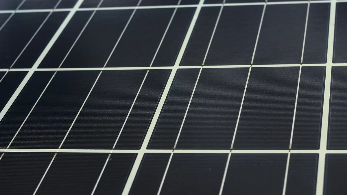 A close-up view of a solar panel, comprising multiple dark gray rectangular cells with white lines separating them.