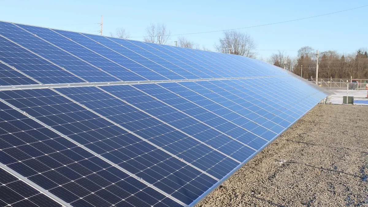 A large array of solar panels installed on a sloping ground.