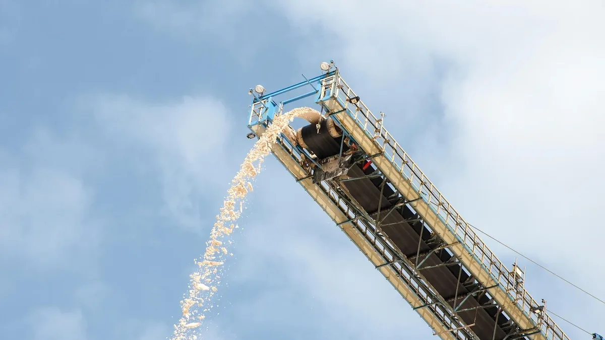 A tall, metal structure with a large pipe at its top, from which a stream of sand is being poured into the air.