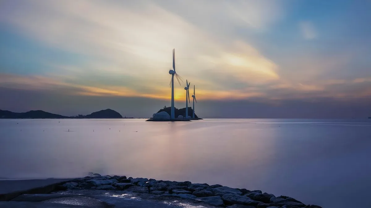 A wind turbine situated on a small island in the middle of a body of water, with a rocky shoreline visible in the foreground.